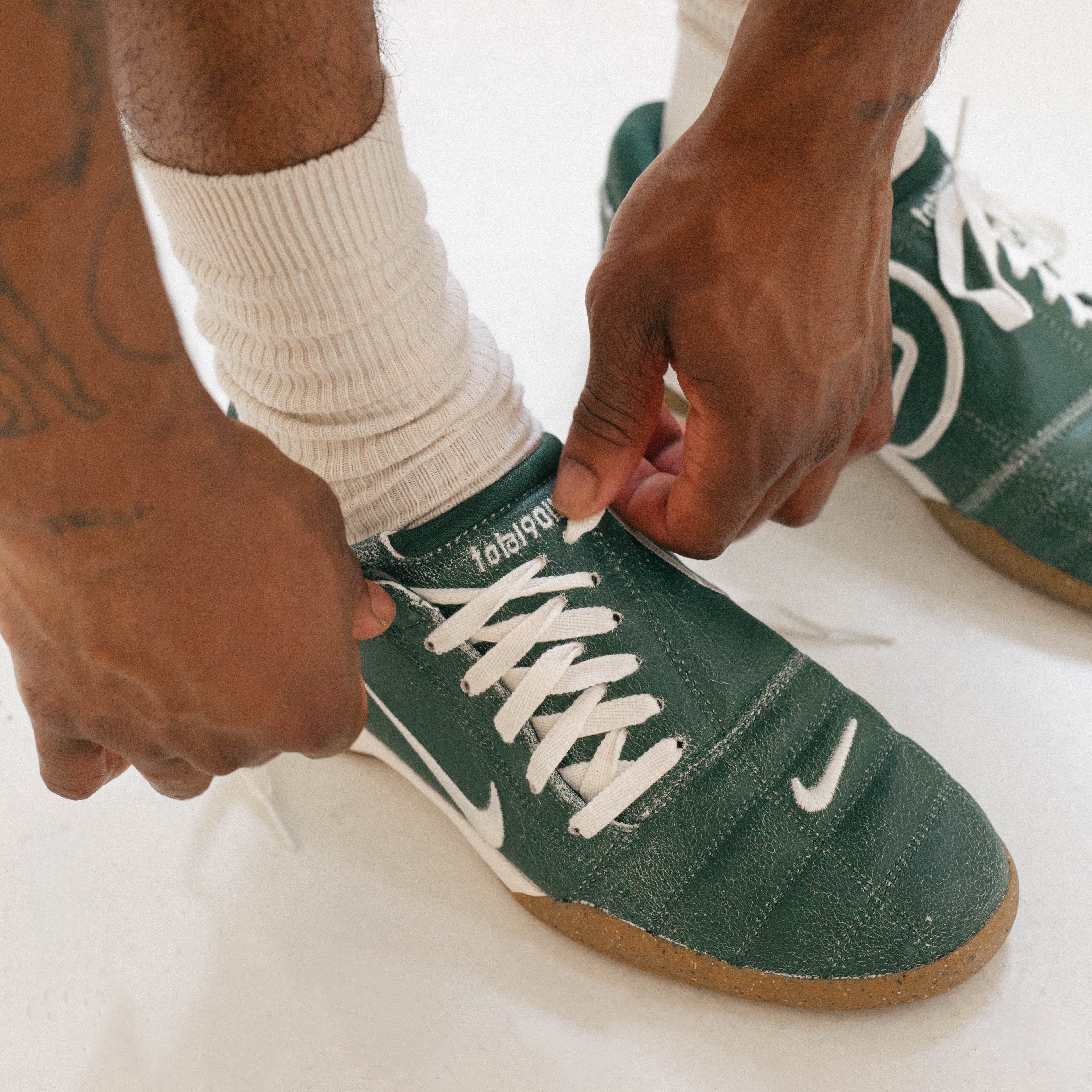 Person wearing green sneakers with white laces on a light background