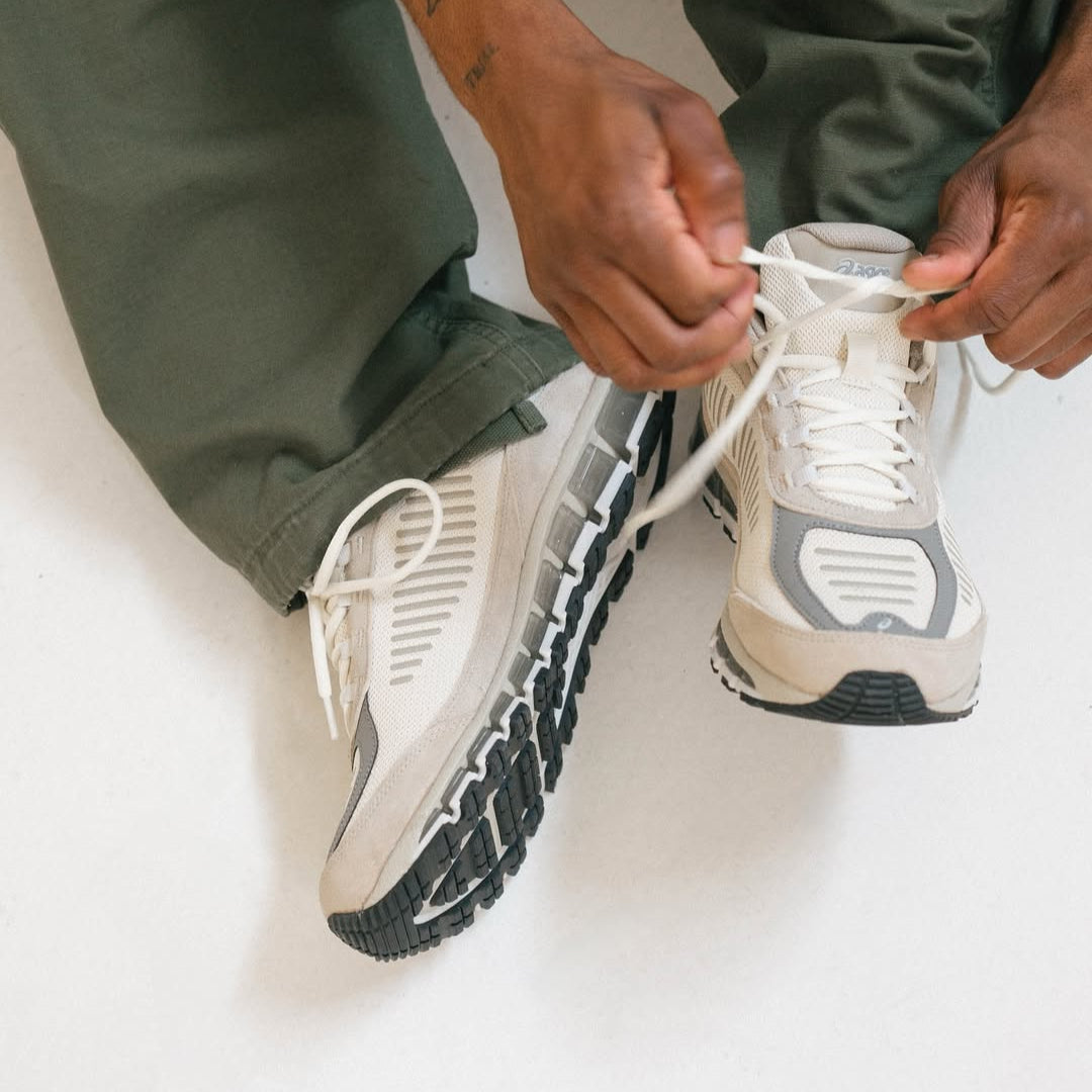 Person tying shoelaces on beige sneakers with a neutral background